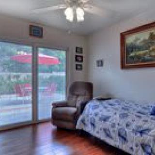 A cozy bedroom featuring a bed with a blue and white quilt, a recliner chair, and large French doors opening to a patio with an umbrella.