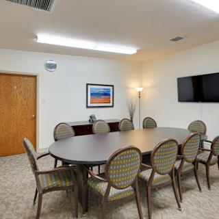 A well-furnished meeting room featuring a large conference table surrounded by chairs, equipped with wall art and a television.