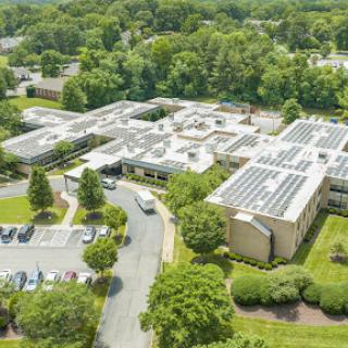 An aerial view of a modern building featuring solar panels surrounded by lush greenery.