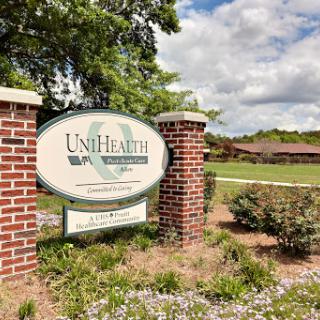 Entrance sign of UniHealth surrounded by landscaped greenery and a cloudy sky.