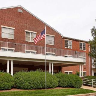 A brick building with an American flag on a pole in front and well-maintained bushes.
