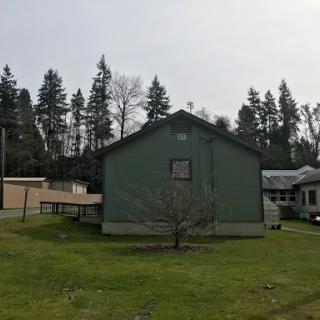 A green house set against a backdrop of trees and an open grassy area.
