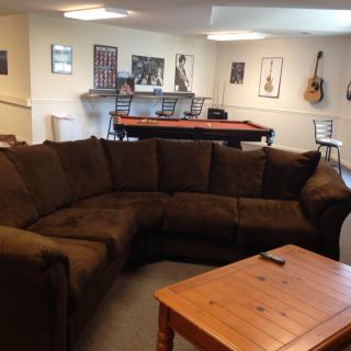A cozy living room with a large sofa, pool table, and wall-mounted guitar.