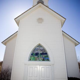 A serene white church adorned with colorful stained glass windows, basking in the bright sunlight.
