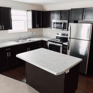 A modern kitchen with dark cabinets, a central island, and stainless steel appliances.