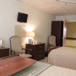 A cozy hotel room with two beds, a lamp, and a wall-mounted television.
