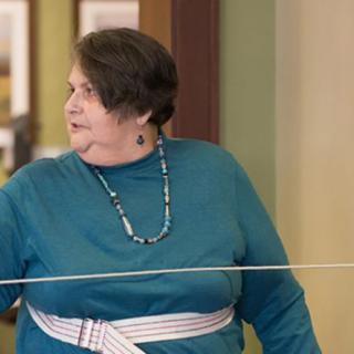 A woman wearing a teal shirt and necklace indoors.