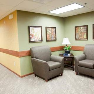A cozy waiting area featuring two comfortable chairs, a small table with a lamp, and framed artwork on the walls.