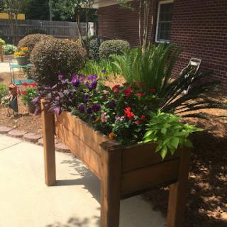 A vibrant wooden planter filled with a variety of colorful flowers, enhancing the beauty of the garden.