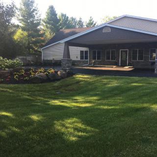 A charming house with a well-maintained lawn and garden, surrounded by trees under the afternoon sunlight.
