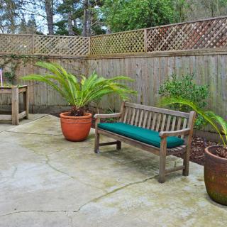 A cozy patio featuring a wooden bench with green cushion, surrounded by potted plants and enclosed by a wooden fence.