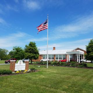 A building with an American flag flying in front, surrounded by greenery on a clear day.