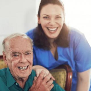 An elderly man sitting with a caregiver, both smiling.