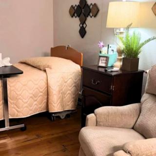A cozy bedroom with a hospital bed, armchair, and side table with a lamp.