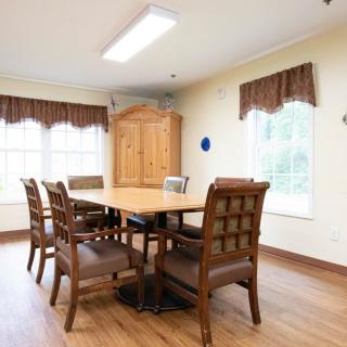 A bright dining room featuring a wooden table and chairs, with large windows and a cabinet.