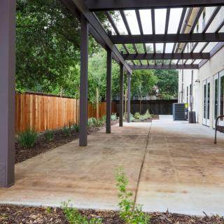 A modern backyard patio with a pergola and surrounding greenery.