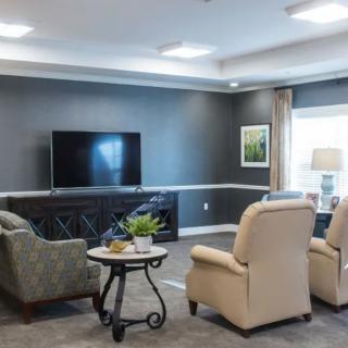A cozy living room featuring comfortable armchairs facing a large television, with a small table in the center.