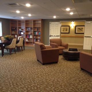 A cozy lounge area featuring comfortable chairs, a round table, and a bookshelf.