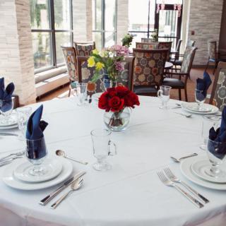 An elegantly set dining table with a white tablecloth, adorned with red and yellow flowers, blue napkins, fine china, and polished silverware.
