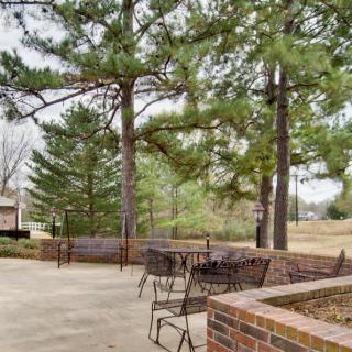 A peaceful outdoor patio area with tables and chairs surrounded by trees and brick walls.