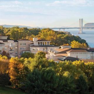 Scenic view of buildings surrounded by lush greenery and a bridge over a river.