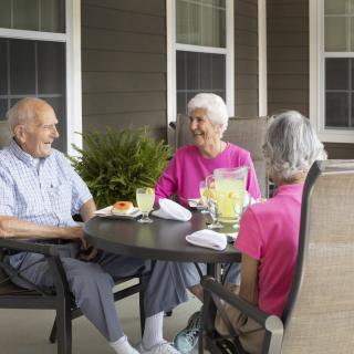 A group of seniors enjoying a casual conversation at a patio table with drinks.