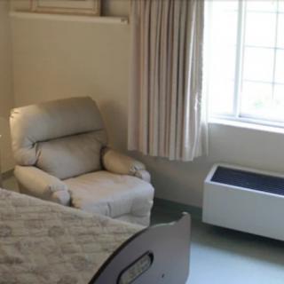 A hospital room featuring a bed, comfortable recliner, and a window with curtains.