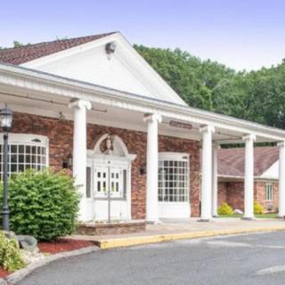A brick building with white columns and a porch set against a backdrop of trees.
