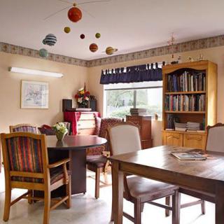 A cozy dining room with a table, chairs, bookshelf, and a model solar system hanging from the ceiling.