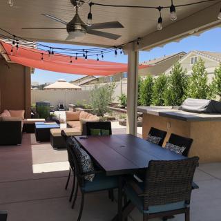 A cozy backyard patio with a dining area, lounge seating, and barbecue under string lights.