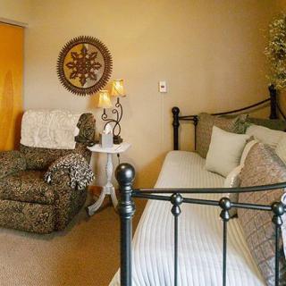 A cozy bedroom featuring a metal-framed bed, plush armchair, soft lighting, and decorative wall art.