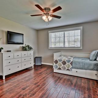 A modern bedroom featuring a daybed, dresser, and television, with hardwood floors and a ceiling fan.