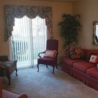 A cozy living room with classic decor, featuring a sofa, armchair, curtains, and an indoor plant.