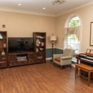 A cozy living room with a television, bookshelf, chair, lamp, and piano next to a large window.