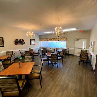 A cozy dining room with multiple tables and chairs, adorned with chandeliers and a wooden floor.