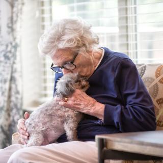 An elderly woman lovingly embraces her small dog on the couch.