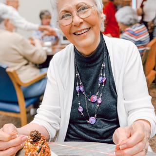 An elderly woman smiling while enjoying a meal at a social gathering.