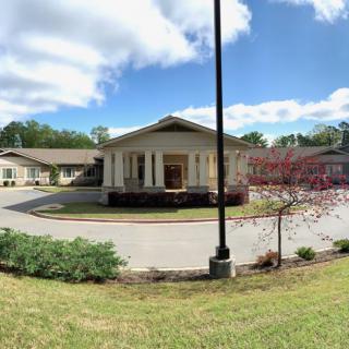 A scenic view of a building with a circular driveway, surrounded by greenery and under a partly cloudy sky.