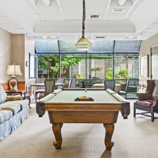 A cozy billiard room with a pool table and comfortable seating, surrounded by large windows.
