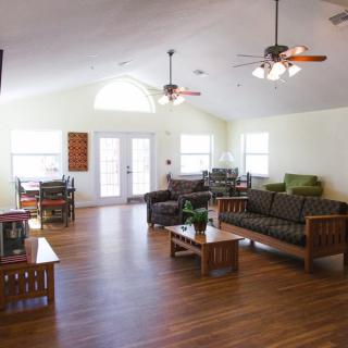 A spacious and bright living room with wooden floors, sofas, ceiling fans, and natural lighting.