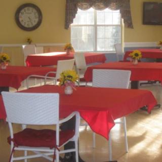 A cozy dining area with tables covered in red tablecloths and sunlight streaming through the window.