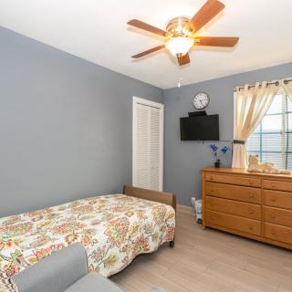 A cozy bedroom with a single bed, wooden dresser, and a ceiling fan.