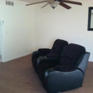 A minimalist living room with two black recliner chairs and a ceiling fan.