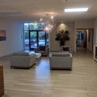 A modern lobby with stylish furniture and a chandelier, featuring ample natural light.