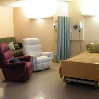 A hospital patient room with a bed and several comfortable chairs.