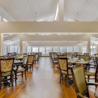 A spacious dining room with neatly arranged tables and chairs, featuring large windows and a hardwood floor.
