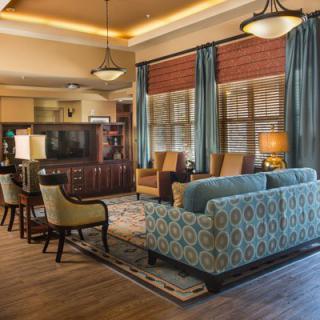 A cozy living room with elegant furniture, featuring a patterned sofa and chairs, wooden flooring, and warm lighting.