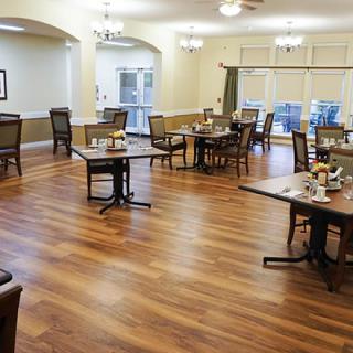 An empty dining room with wooden floors and neatly arranged tables and chairs.