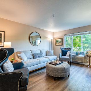 A cozy and stylish living room featuring a comfortable sofa, armchairs, an ottoman, and decorative elements like a mirror and artwork.