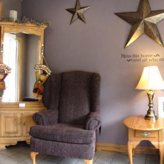 A cozy living room corner with a plush armchair, wooden side table and lamp, star wall decorations, and a mirror.